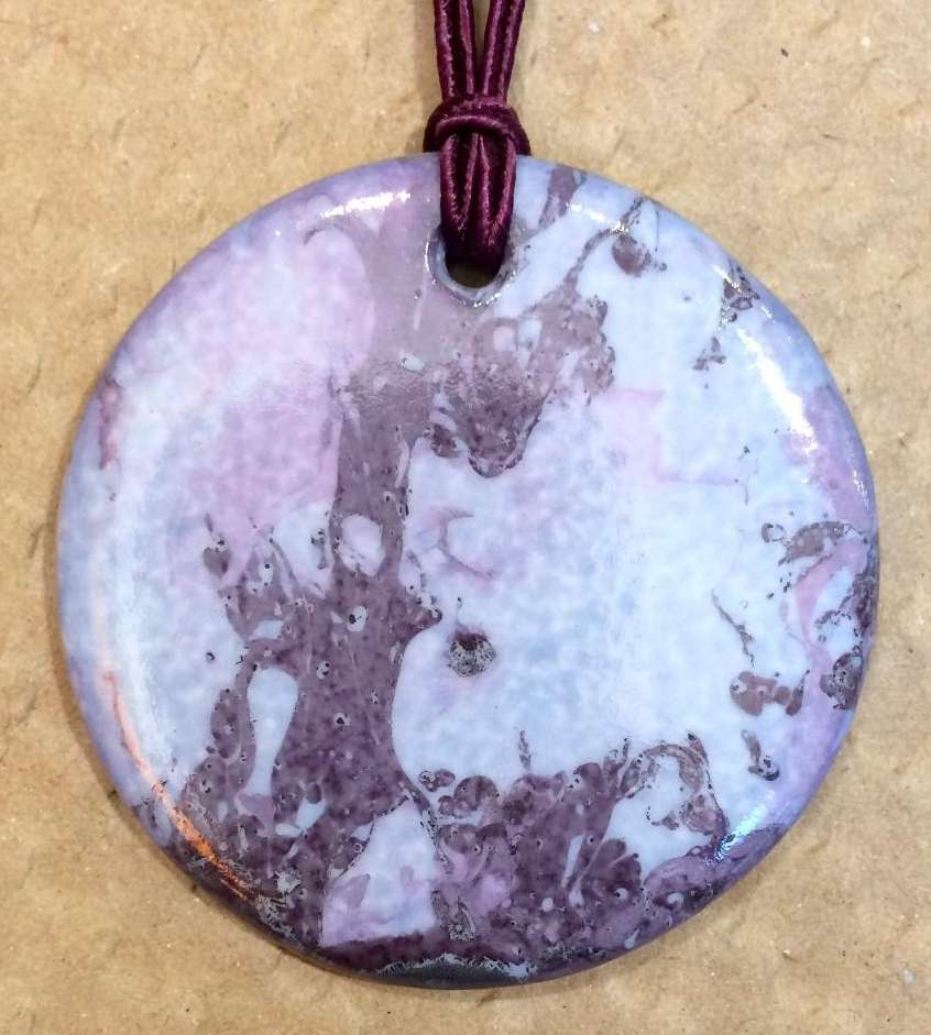 Pendentif rond en porcelaine personnalisé par un fond violet-parme.